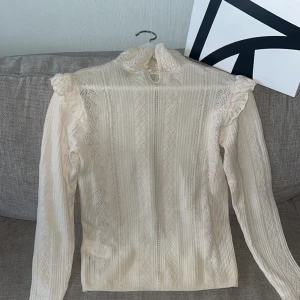 Ralph Lauren  - Ralph Lauren beige blus med spets och volangdetaljer på axlarna. Hög hals med knapp i nacken och långärmad modell. Nypris 2499kr. Skick 10/10       