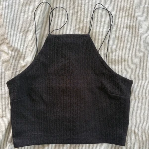 Svart croppad topp Gina Tricot - Svart croppad linnetopp från Gina Tricot med tunna axelband och hög halsringning. Perfekt till fest!