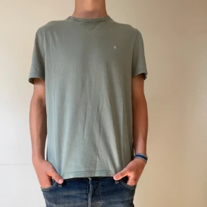 Grön t-shirt från Morris - Snygg grön t-shirt i enkel design med liten broderad logga på bröstet. T-shirten har rund hals och korta ärmar, perfekt för en avslappnad stil. Materialet känns mjukt och skönt mot huden, och passformen är normal. Enkelt plagg som funkar till det mesta. Modellen är 174!