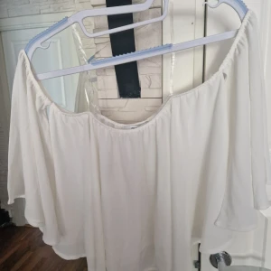 Vit offshoulder blus från Chiquelle - Supersöt vit offshoulder blus från Chiquelle i flowy material. Vida ärmar och rynkad resår upptill ger en luftig och romantisk vibe. Perfekt till jeans eller kjol när du vill ha en chill men ändå snygg look.