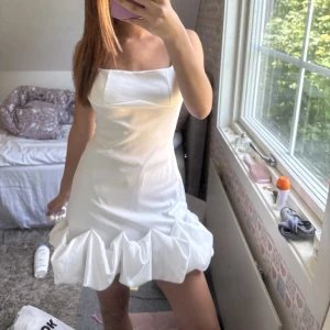 Vit kort klänning med volangkant - Superfin vit kortklänning med breda axelband och unik volangkant längst ner. Klänningen har en enkel, stilren design och är perfekt för dig som gillar en clean look med en twist. Snygg till fest