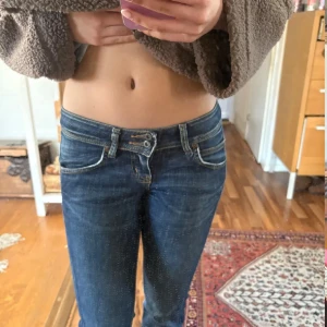 Mörkblå lågmidjade jeans från Lee - Säljer ett par mörkblå jeans från Lee med låg midja. Jeansen har klassiska fem fickor, dubbla knappar i midjan och snygga slitningar. Perfekta för dig som gillar en tidlös och avslappnad look.