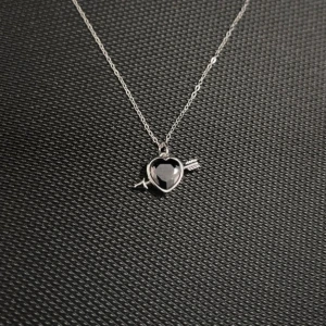 L’Amour Noir – Silver Necklace with Heart and Arrow - Silverpläterat halsband i rostfritt stål med ett svart hjärta genomborrat av en pil. Justerbar längd 40 + 5 cm