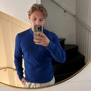 Blå pikétröja från GANT i bomull - Säljer en klassisk blå pikétröja från GANT i mjuk bomull. Tröjan har lång ärm, krage och tre knappar framtill. Broderad GANT-logga på bröstet. Perfekt för dig som gillar stilrena och tidlösa plagg.