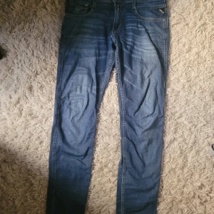 Blå Replay Anbass jeans herr - Snygga blå Replay Anbass jeans i klassisk denim med lätt slitning och raka ben. Modellen har fem fickor, normal passform och är tillverkad i mjukt bomullsmaterial med stretch. Perfekta för dig som gillar stilrena och bekväma jeans.