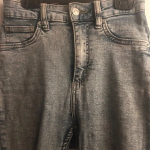 Ljusgrå skinny jeans med råa kanter - Säljer ett par ljusgrå skinny jeans med snyggt slitna, råa kanter nertill. Jeansen har klassisk femficksdesign, hög midja och är tillverkade i mjukt denim. Perfekta för dig som gillar en avslappnad men trendig look.