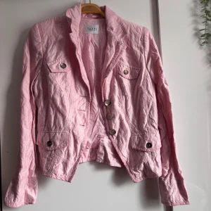 Ljusrosa Kavaj/Jacka Tuzzi - Snygg ljusrosa kavaj/jacka från Tuzzi med klassisk krage, fyra fickor med knappar framtill. Jackan är tillverkad i bomull och har en figurnära passform. Perfekt för dig som vill ha en feminin och trendig look. Enda defekten är väll att den är skrynklig men det går såklart att fixa med ett strykjärn! Ingen storlek men skulle säga S-M🤗
