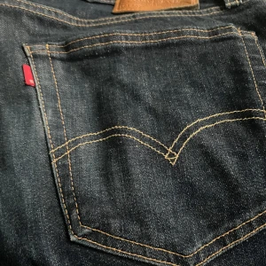Levi's 502 mörkblå jeans W34 L30 - Säljer ett par Levi's Premium 502 jeans i mörkblå denim. Klassisk femficksmodell med snygga kontrastsömmar och läderpatch bak. Jeansen har en rak passform och är tillverkade i slitstarkt bomullstyg. Perfekta för en clean och tidlös look.