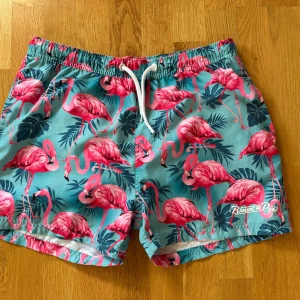 Badshorts - Hej, Säljer 3 par badshorts. Köptes förra året och ej använda mycket, säljs nu då jag växt ur dom över vintern. Därför i bra skick.  Ett par turkosa med rosa flamingos och gröna blad från Blount & Pool i storlek L. 40kr.  Ett par gula från HM i storlek S. Pris 30kr. Ett par orange från SOC i storlek M. Pris 40kr.