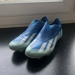Adidas blå fotbollsskor Crazyfast - Säljer ett par Adidas Crazyfast fotbollsskor i blått med vita ränder och orange dobbar. (Hel Äkta) Skorna har en strömlinjeformad design utan snörning och är tillverkade i syntetmaterial för lätt känsla och bra grepp på planen. Har tyvärr inte kvar sulorna med det är enkelt att lösa! Skriv gärna vid frågor eller funderingar🌟