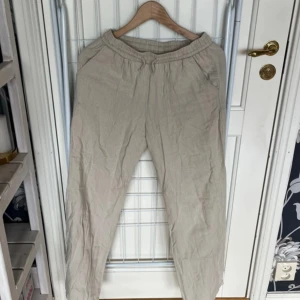 Beiga linnebyxor från Lindex, strl 164 - Snygga och luftiga beiga linnebyxor från Lindex med resår i midjan och sidfickor. Perfekta för chill dagar eller när du vill ha en avslappnad stil. Byxorna är raka i modellen och gjorda i skönt linnematerial.