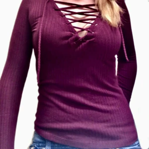 Vinröd ribbad topp med snörning Bershka - Vinröd långärmad topp från Bershka i ribbad bomullsmix. Snygg snörning framtill med v-ringning. Figurnära passform och mjukt stretchigt material, perfekt till jeans eller kjol.