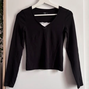 Svart långärmad topp med spets - Svart långärmad topp från House med v-ringning, liten rosett framtill och vit spetskant vid halsen. Sitter snyggt och har en normal passform. Använd en gång🤗