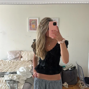 Svart volangblus från Zara - Supersöt svart blus från Zara med volanger och spetsdetaljer. Djup v-ringning och korta ärmar med volang ger en romantisk vibe. Blusen är figurnära och har stickad nederkant som sitter snyggt i midjan. Perfekt att styla med jeans eller kjol.. pris kan diskuteras