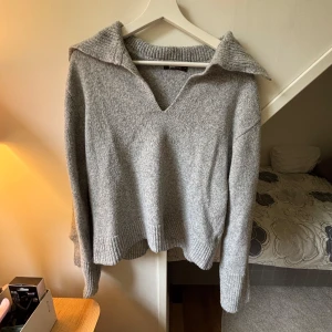 Grå stickad tröja med krage - Mysig grå stickad tröja från Gina Tricot med bred krage och v-ringning. Tröjan har långa ärmar och ribbade muddar vid ärmslut och nederkant. Jättebra skick! 
