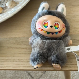 Labubu - Supersöt och unik gosedjur till väska i form av ett monster med grå fluffig päls, stora öron och regnbågsfärgade ögon. Labubu har färgglada detaljer runt munnen och är perfekt för dig som vill sticka ut. Märke: The Monsters. Pop Mart