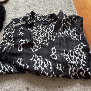 Svartvit leopardmönstrad blus Fransa - Säljer en svartvit blus från Fransa i storlek S med coolt leopardmönster. Blusen är ärmlös och har en snygg v-ringning samt en detalj med små glittriga stenar på axeln. Perfekt för dig som vill sticka ut lite extra.