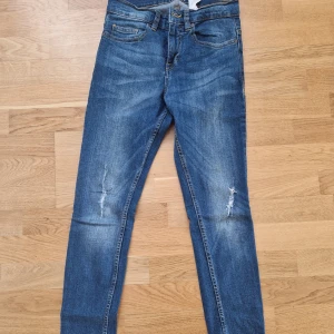 Blå skinny jeans från Pull&Bear - Säljer ett par blå skinny jeans från Pull&Bear med slitningar på knäna och klassisk femficksdesign. Jeansen har en smal passform och är tillverkade i stretchig denim för extra komfort. Perfekta för dig som gillar en tajt look.