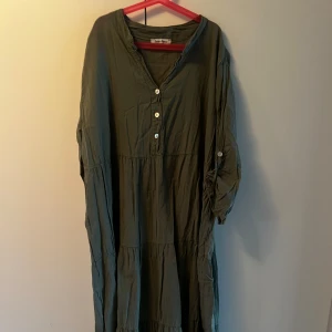 Grön långklänning från Zanca Sonne - Luftig grön långklänning från Zanca Sonne med v-ringning, knappar framtill och långa ärmar som kan rullas upp och fästas med knapp. Klänningen har en avslappnad passform och är tillverkad i mjuk bomull. Katt finns i hemmet, kontakta vid fler frågor🌷