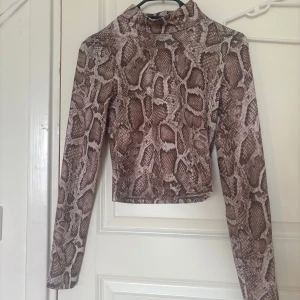 Brun croppad turtleneck med ormmönster - Säljer en brun turtleneck med orm mönster ifrån hm, helt oandvänd🌼