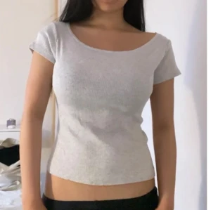 Ljusgrå ribbad topp med kort ärm - Enkel och stilren ljusgrå topp med ribbad struktur och korta ärmar. Toppen har en bred, rundad urringning som ger en snygg offshoulder-look. Sitter figurnära och är perfekt att matcha med jeans eller kjol.