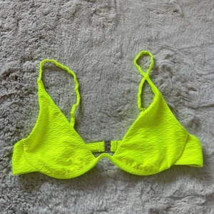 Neongul bikiniöverdel med struktur - Snygg neongul bikiniöverdel med vågig struktur och smala axelband. Bikinin har bygel och spänne bak för extra support. Perfekt för dig som vill sticka ut på stranden med en riktigt poppig färg. Storlek M men passar även storlek S