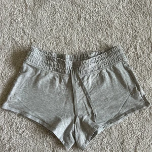 Grå shorts från Victoria’s Secret  Sport - Grå mjuka shorts från Victoria’s Secret Sport med elastisk midja och snörning framtill. Perfekta för träning eller chill dagar. Tillverkade i bomullsmix för en skön och avslappnad känsla.