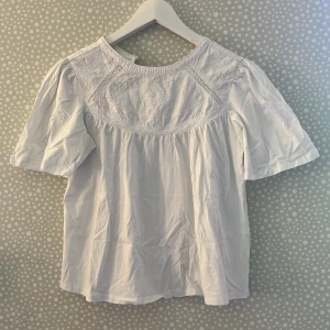 Vit blus med broderi från Zara - Supersöt vit blus från Zara med broderade detaljer och korta puffärmar. Blusen har rund halsringning och fina spetsinslag upptill. Perfekt för dig som gillar romantisk och luftig stil. Tillverkad i mjuk bomull som känns skön mot huden.