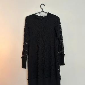 Svart spetsklänning med lång ärm - Svart klänning med spetsmönster och långa ärmar. Modellen är rak och slutar ovanför knäna. Ärmsluten och nederkanten har ribbade detaljer som ger en cool kontrast till spetsen. Aldrig blivit använd och har prislappen kvar. 