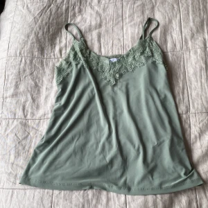 Grön linnetopp med spets från Amisu - Snygg ljusgrön linnetopp från Amisu i storlek XS. Toppen har tunna axelband och v-ringning med fina spetsdetaljer framtill.