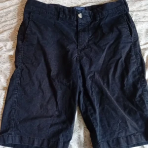 Svarta shorts från Morris - Klassiska svarta shorts från Morris med normal passform. De har fickor fram och bak, bälteshällor och stängs med knapp och dragkedja. Perfekta för sommaren och enkla att matcha med det mesta. Snygg och stilren look.