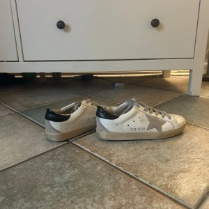 Golden Goose Superstar sneakers stl 37 - Golden Goose Superstar sneakers i vitt skinn med grå mockastjärna på sidan och svarta detaljer vid hälen. Storlek 37. Box finns.