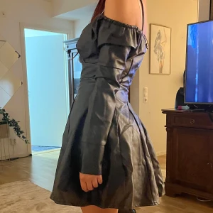 Nakd Svart offshoulder kort klänning - Supersnygg svart kort klänning med offshoulder och långa ärmar. Klänningen har v-ringning och markerad midja som ger en riktigt fin siluett. Materialet har en lätt glansig finish som ger en cool look. Perfekt för dig som vill sticka ut!