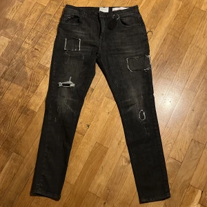 Svarta skinny jeans från Amicci, stl 34 - Svarta jeans från Amicci med skinny fit och slitna detaljer samt patchade partier på benen. Snyggt tvättad look och klassisk femficksmodell. Jeansen har dragkedjegylf och är tillverkade i ett stretchigt bomullsmaterial.   (Pris kan diskuteras)