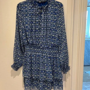 klänning från Zara - Supersöt blå och vit kortklänning från Zara med mönster, långa ärmar och smock i midjan. Klänningen har volangdetaljer nertill och knytning vid halsen. Perfekt för dig som gillar färg och mönster! Använd fåtal gånger!💙