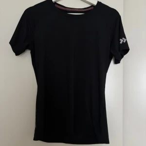 Svart tränings-tshirt från Lager 157 - Svart t-shirt från Lager 157 i sportig modell med korta ärmar och liten slits i sidan. Tillverkad i mjukt och lätt polyestermaterial som andas, perfekt för träning. Diskret logga på ärmen och insidan av kragen.