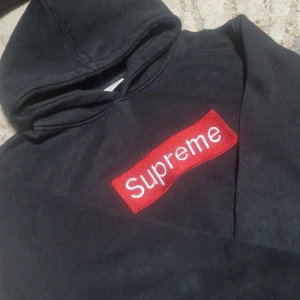 Supreme Hoodie - Supreme hoodie i svart med ikonisk röd boxlogo på bröstet. Klassisk streetwear-stil med huva och långa ärmar.