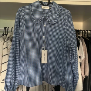 Blårutig skjorta med volangkrage - Snygg blårutig skjorta från Carin Western med volangdetaljer på kragen och klassiska knappar framtill. Aldrig använd och har prislapp kvar, nypris 499❣️❣️