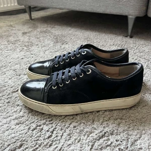 Mörkblåa skor från Lanvin med lackad tå - Snygga mörkblå sneakers från Lanvin med klassisk design. Ovandel i mocka och tåparti i blankt lackskinn, vita gummisulor och mörkblåa snören. Perfekta för dig som gillar stilrena och exklusiva sneakers med en twist.
