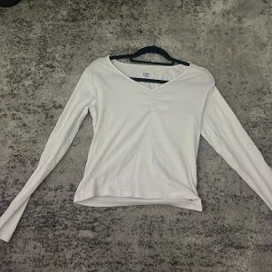 Vit långärmad topp med v-ringning 157 - Säljer en stilren vit långärmad topp från 157 med v-ringning och lätt rynkdetalj framtill. Modellen är figurnära och passar perfekt till jeans eller kjol. Mjuk och skön bomullskänsla, enkel att matcha och superfräsch i garderoben.