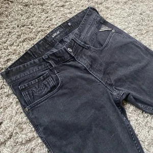 Svarta Replay jeans slim fit  - Säljer ett par svarta Replay jeans med slim passform. Klassisk femficksmodell med snygga detaljer på bakfickan och metallmärke på myntfickan. Jeansen är i stretchigt denim som sitter tajt och bekvämt. Perfekta för dig som gillar en stilren look.