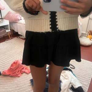 Svart volangkjol med smock - Supersöt svart kortkjol med bred smock i midjan och dubbla volanger. Kjolen är i ett lätt, skönt tyg som ger en flowig känsla och passar perfekt till sneakers eller boots. Enkel att matcha och riktigt bekväm att bära. Kan bäras både som topp och kjol, går även att vika ner smocken för att få den mer lågmidjad 🥹❣️