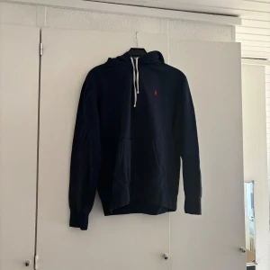 Marinblå hoodie från Ralph Lauren - Säljer en marinblå hoodie från Ralph Lauren med vit snörning i huvan och klassisk röd logga på bröstet.  Passar M och L