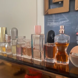 Mixade miniparfymer från kända märken - Säljer ett set med flera miniparfymer från märken som Estée Lauder, Yves Rocher, Giorgio Armani och Jean Paul Gaultier. Flakongerna är i glas med olika former och färger, från klassiskt rektangulära till kroppsinspirerade designer. Färgerna varierar mellan klara, rosa, guld och bärnstensfärgade toner.