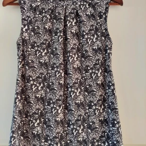 Blommig topp/blus från Stockh LM - Supersöt blus/toppfrån Stockh LM i svartvitt blommigt mönster. Ärmlös modell med rund halsringning och dragkedja bak. Perfekt för dig som gillar en stilren men ändå lekfull look.