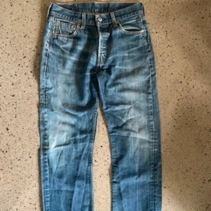 Levi's 501 blå jeans W30 L34 - Klassiska Levi's 501 jeans i blå tvätt med raka ben och normal passform. Jeansen har fem fickor, knappgylf och snygga slitningar för en vintage-look.