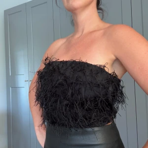 Svart bandeau tubtopp från Gina Tricot - Säljer en svart bandeau tubtopp från Gina Tricot med coola fransdetaljer över hela framsidan. Toppen är axelbandslös och har dragkedja bak för enkel påklädning. Perfekt för dig som vill sticka ut med en edgy och trendig look.