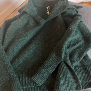 Mörkgrön stickad tröja Gina Tricot - Mysig mörkgrön stickad tröja från Gina Tricot med krage och breda ribbade muddar. Perfekt för lager-på-lager och chill höst- eller vinterstil. Tröjan har lång ärm och en loose fit som ger en avslappnad vibe.