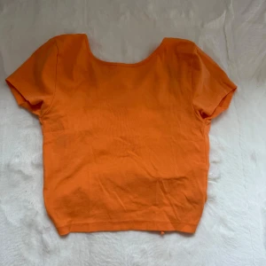 Orange croppad topp med knyt i ryggen - Säljer en orange croppad topp med korta ärmar och snyggt knyte i ryggen. 