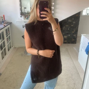 Mörkbrun stickad väst med slits - Säljer en lång, mörkbrun stickad väst med hög hals, armpuffar och slitsar i sidorna. Västen är ärmlös och har en rak, loose passform som kan stylas med eller utan bälte i midjan. Från H&M i storlek XS❤️